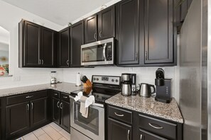 A modern kitchen with dark cabinetry, stainless steel appliances, and a granite countertop. - Modern 6BRPoolVilla w/HotTub &GameRoom Near Disney (Kissimmee)