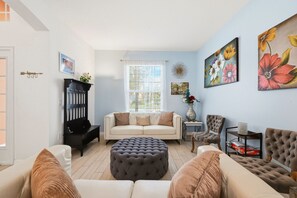 Uma sala de estar com sofá, pufê, poltronas, mesa de centro, lareira e janela com persianas.