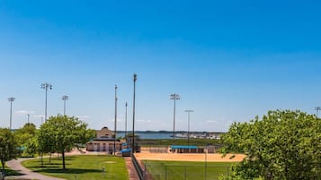 Ein Baseballfeld mit einem Gebäude im Hintergrund, wolkenlosem Himmel und einem Gewässer.