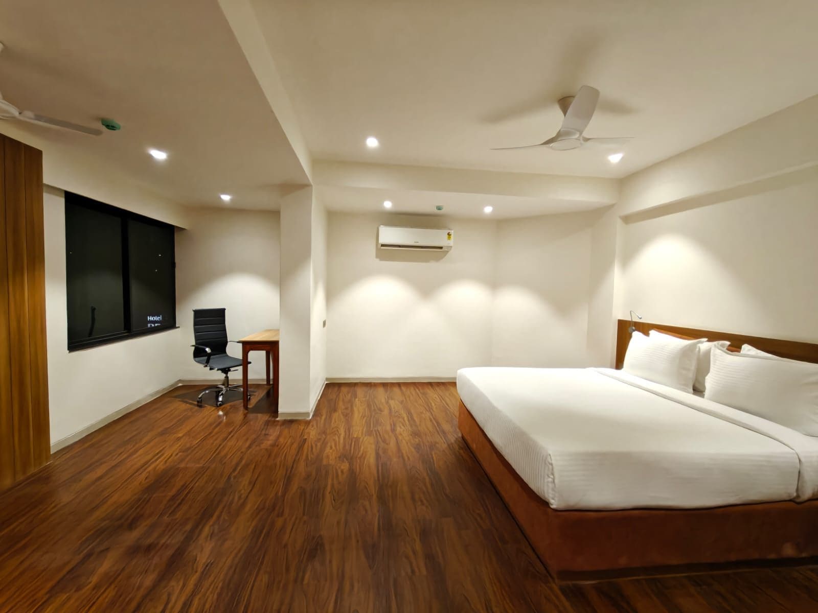 A hotel room with a bed, a desk, a chair, and a window.