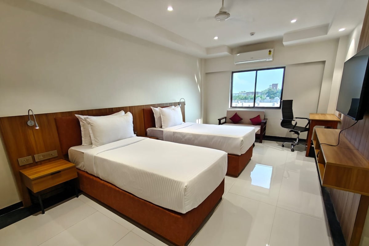 Habitación de hotel con dos camas, un escritorio, una silla, un televisor y una ventana con vistas.