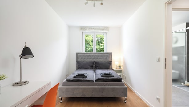 Una camera da letto con un letto, una scrivania, una sedia, una lampada e una finestra.