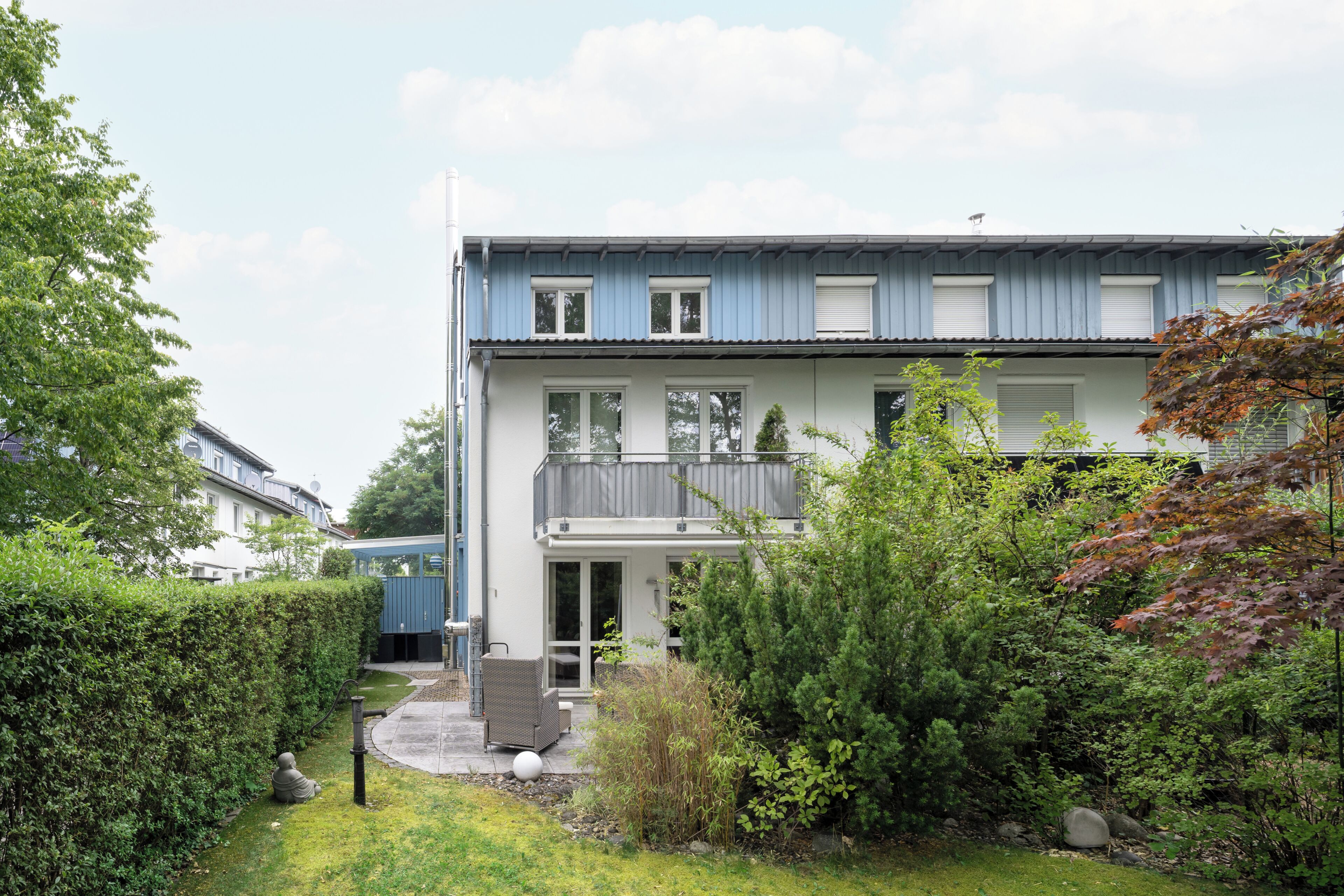 A two-story residential building with a balcony, a covered outdoor seating area, and a well-maintained garden.