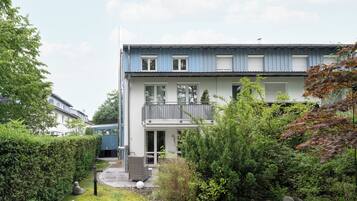 A two-story residential building with a balcony, a covered outdoor seating area, and a well-maintained garden.