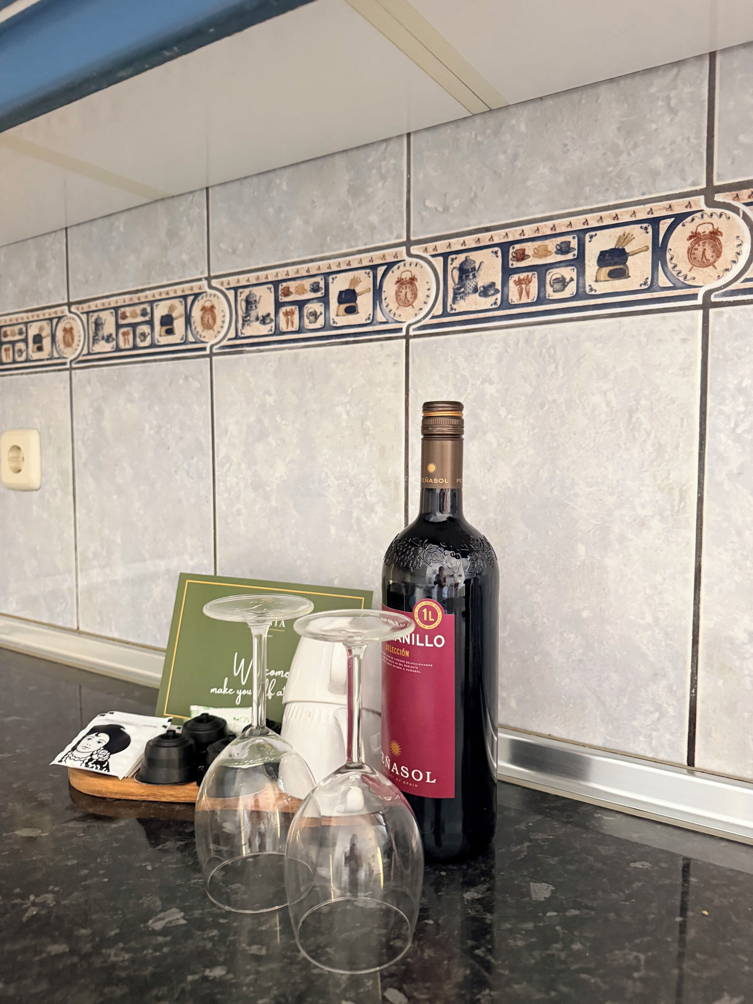A kitchen counter with a wine bottle, glasses, and a decorative tile backsplash.