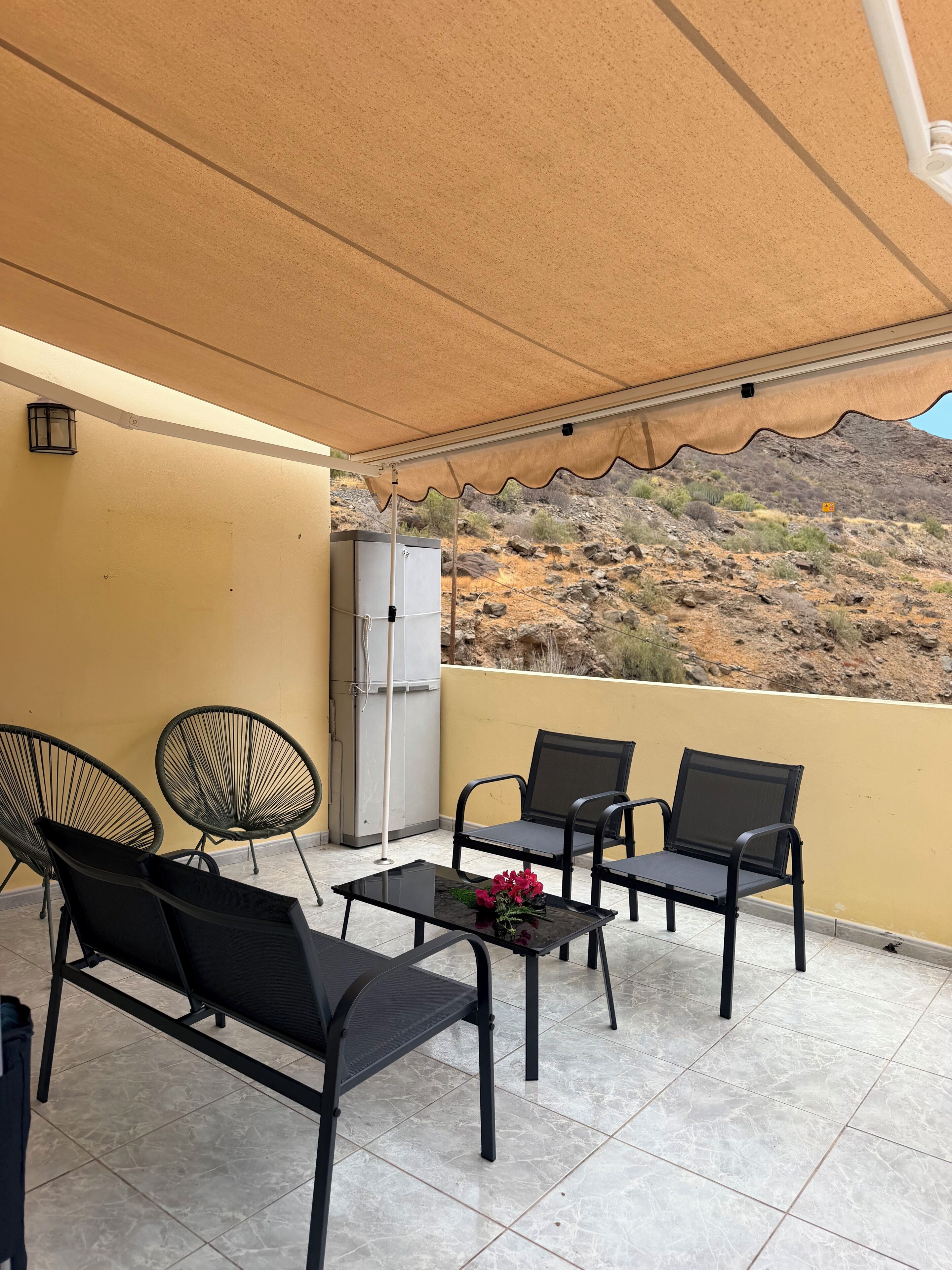 Un balcón con mobiliario exterior, refrigerador y vistas a un promontorio rocoso.