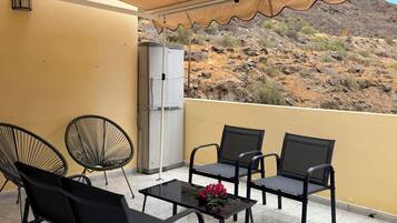 Un balcón con mobiliario exterior, refrigerador y vistas a un promontorio rocoso.