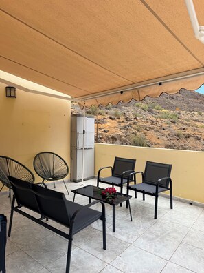 A balcony with outdoor furniture, a refrigerator, and a view of a rocky hillside.