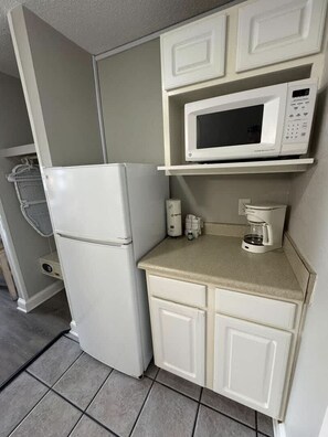 Eine kleine Küchenzeile mit einem weißen Kühlschrank, einer Mikrowelle, einer Kaffeemaschine und einem kleinen Waschbecken.