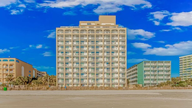 A high-rise hotel with multiple balconies, a flat roof, and a clear blue sky. - Sea Mist 51112 Ocean View Vacation Rental (Myrtle Beach)