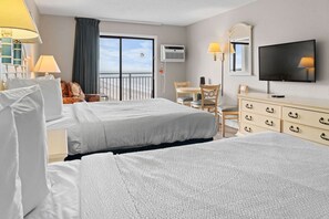Ein Hotelzimmer mit zwei Betten, einem Schreibtisch, einem Stuhl, einem Schminktisch, einem Fernseher und einem Balkon mit Blick.