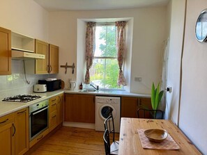A compact kitchen with a gas stove, oven, microwave, and a washing machine. - Leafy Marchmont 2-Bed · Meadows · City Centre (Edinburgh)