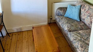 Huoneessa on puulattia, kuviollinen verhoilu, sininen koristetyyny, maisemamaalaus ja seinällä kolme pientä kehystettyä kuvaa.