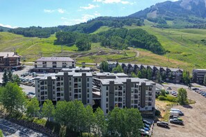 A multi-story residential building with a parking lot and a mountainous backdrop. - Ski Lodge Styled Plaza Condo 3 Bedroom Condo (Crested Butte)