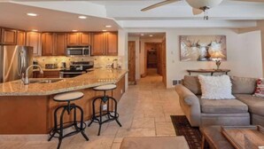 A spacious kitchen with a central island, bar stools, a dining area with a sofa, and a large window providing natural light. - Ski Lodge Styled Plaza Condo 3 Bedroom Condo (Crested Butte)