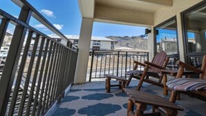 A balcony with wooden chairs and a table, a metal railing, and a view of buildings and hills. - Ski Lodge Styled Plaza Condo 3 Bedroom Condo (Crested Butte)