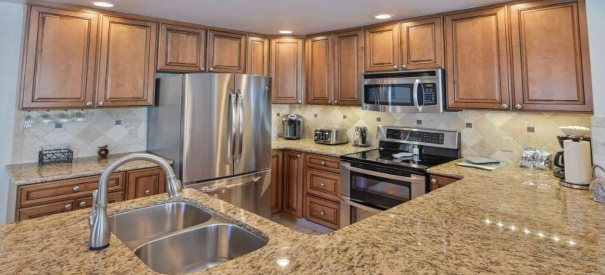 A kitchen with granite countertops, stainless steel appliances, wooden cabinets, and a double sink.