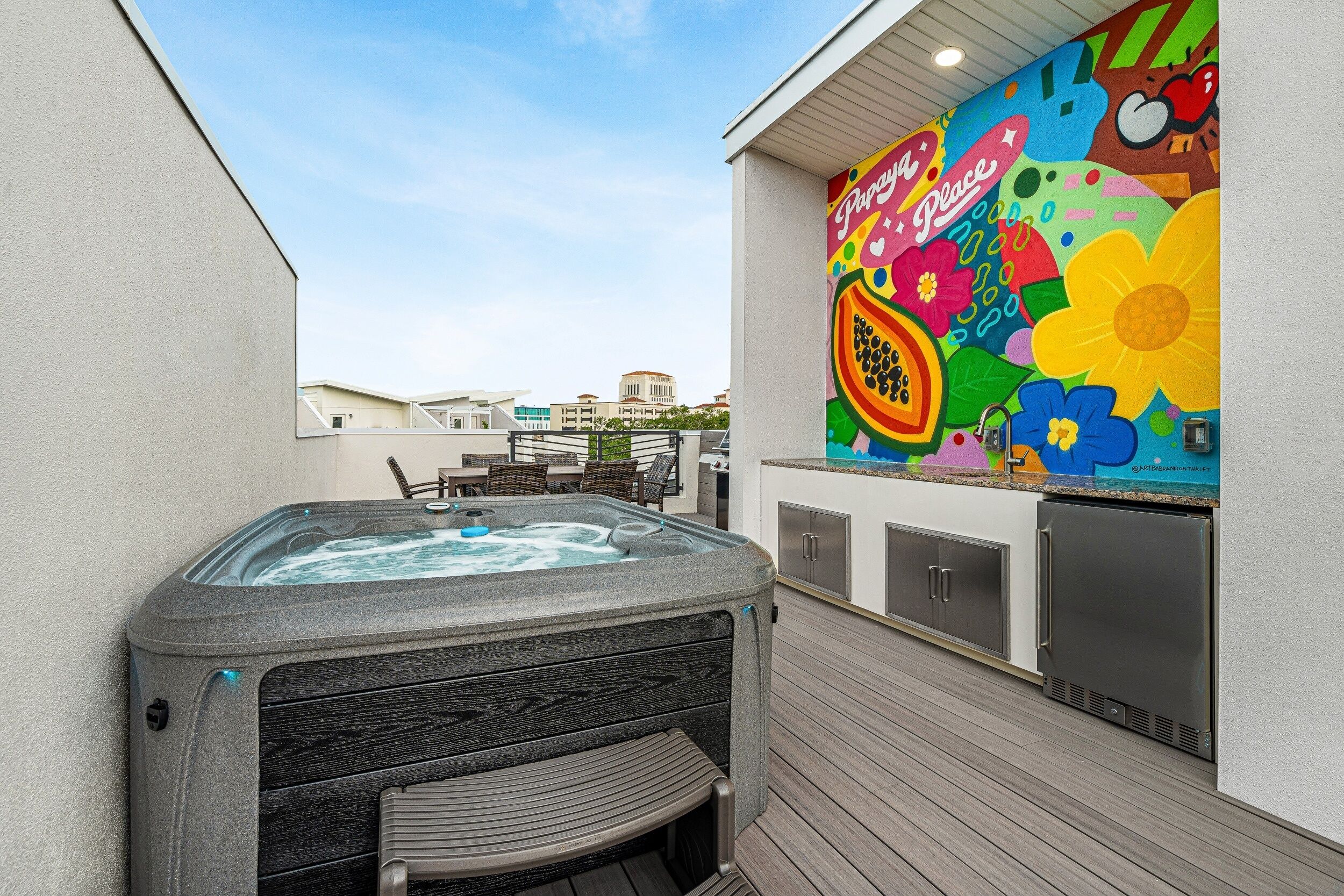 Un bain à remous sur une terrasse en bois, avec une fresque colorée sur le mur adjacent.