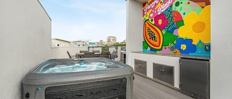 Un bain à remous sur une terrasse en bois, avec une fresque colorée sur le mur adjacent.