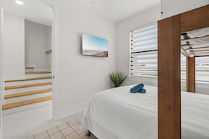 A bedroom with a bed, a window with blinds, a plant, and a wall-mounted TV. - Papaya Place 2 Bedroom Townhouse (Sarasota)