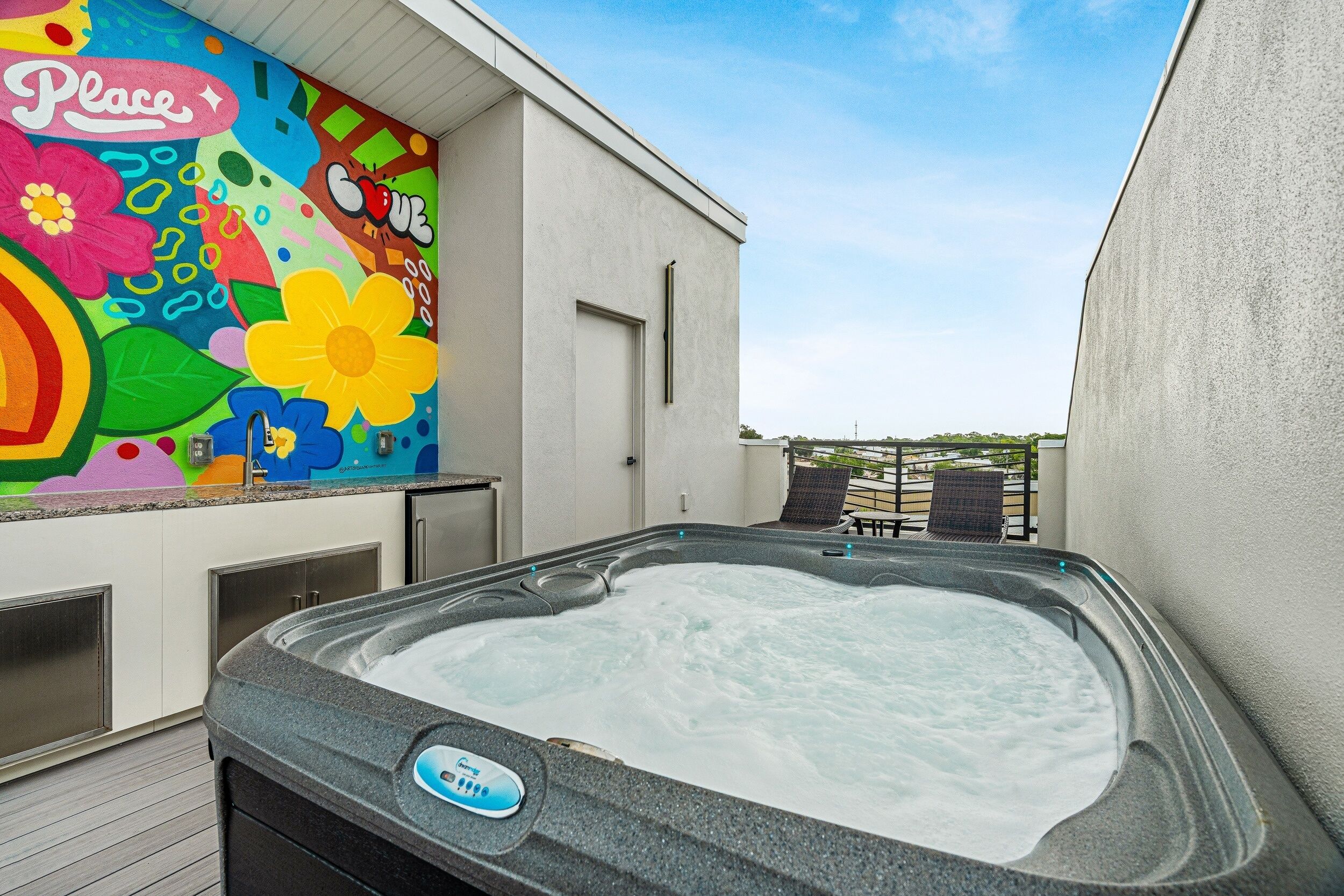 Ein Whirlpoolbereich mit farbenfroher Wandmalerei, blauem Himmel und Blick auf die umliegende Landschaft.