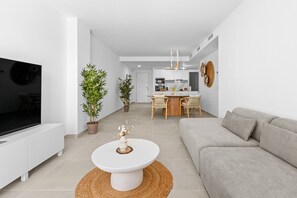 A modern living room with a flat-screen TV, a white coffee table, a beige sofa, and two potted plants. - 13 - Modern 2BR near Cala de Mijas (La Cala de Mijas)