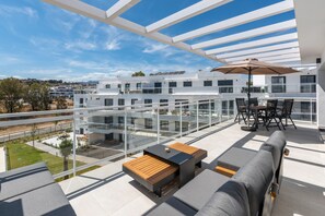 A modern outdoor patio with a glass balustrade, a wooden table, and a sofa. - 13 - Modern 2BR near Cala de Mijas (La Cala de Mijas)