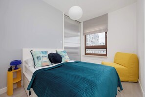 Ein Schlafzimmer mit Bett, Nachttisch, Stuhl, Fenster und einer Pendelleuchte.