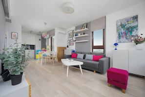 Ein modernes Wohnzimmer mit einem grauen Sofa, einem weißen Couchtisch und einem leuchtend rosa Pouf.