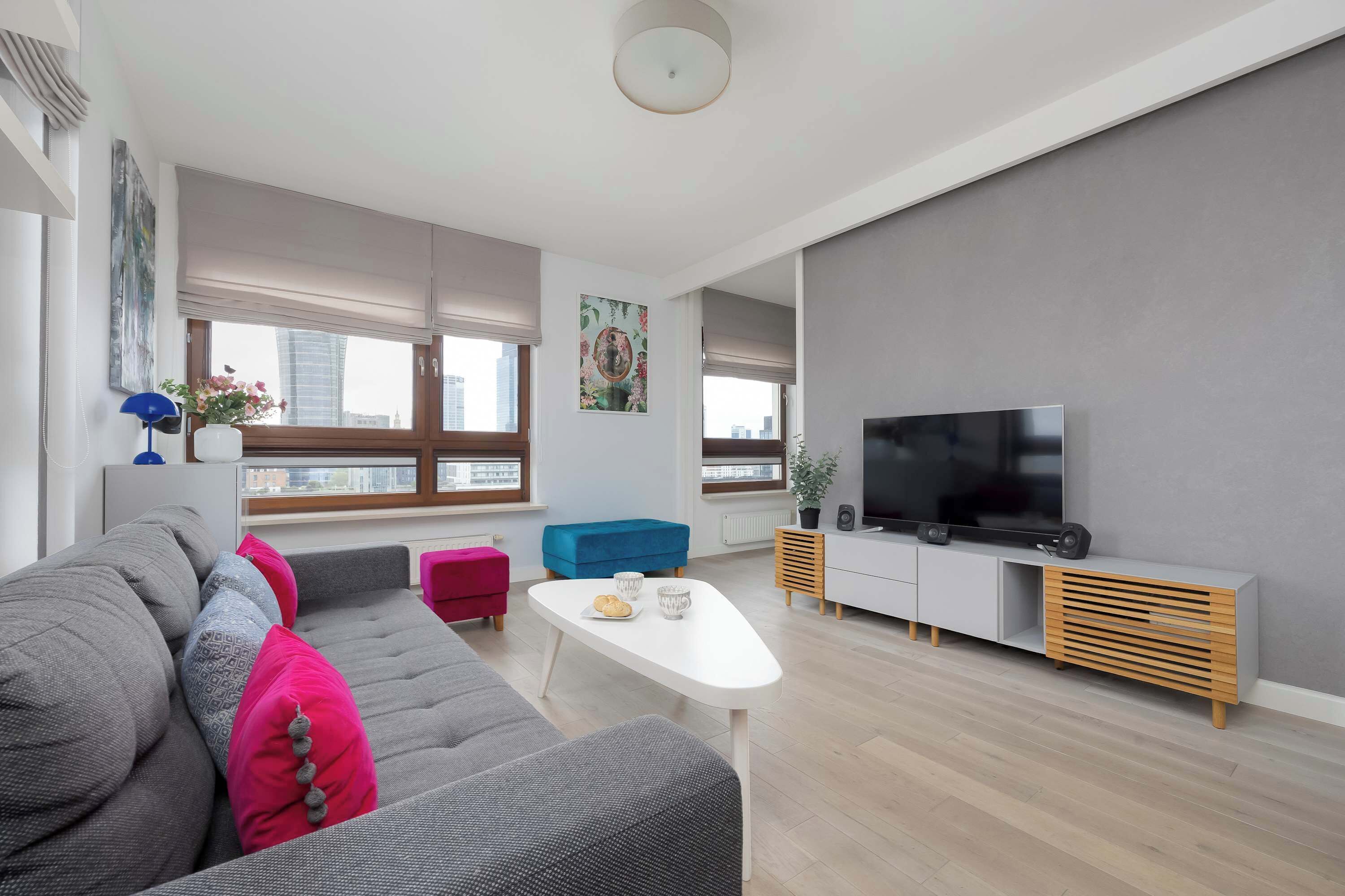 Un salon moderne avec un canapé gris, une table basse blanche et un téléviseur à écran plat posé sur un meuble en bois.