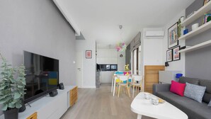 Una sala moderna con televisor de pantalla plana, un sofá, una mesa de comedor con sillas y una cocina al fondo.