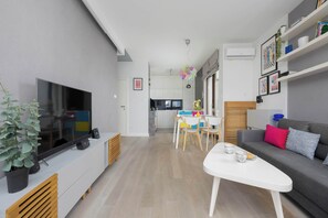 Ein modernes Wohnzimmer mit Flachbildfernseher, einer Couch, einem Esstisch mit Stühlen und einer Küche im Hintergrund.