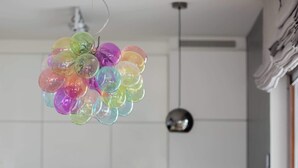 Comedor con una mesa preparada para dos personas, sillas, un florero con flores amarillas y una decoración de globo de colores.