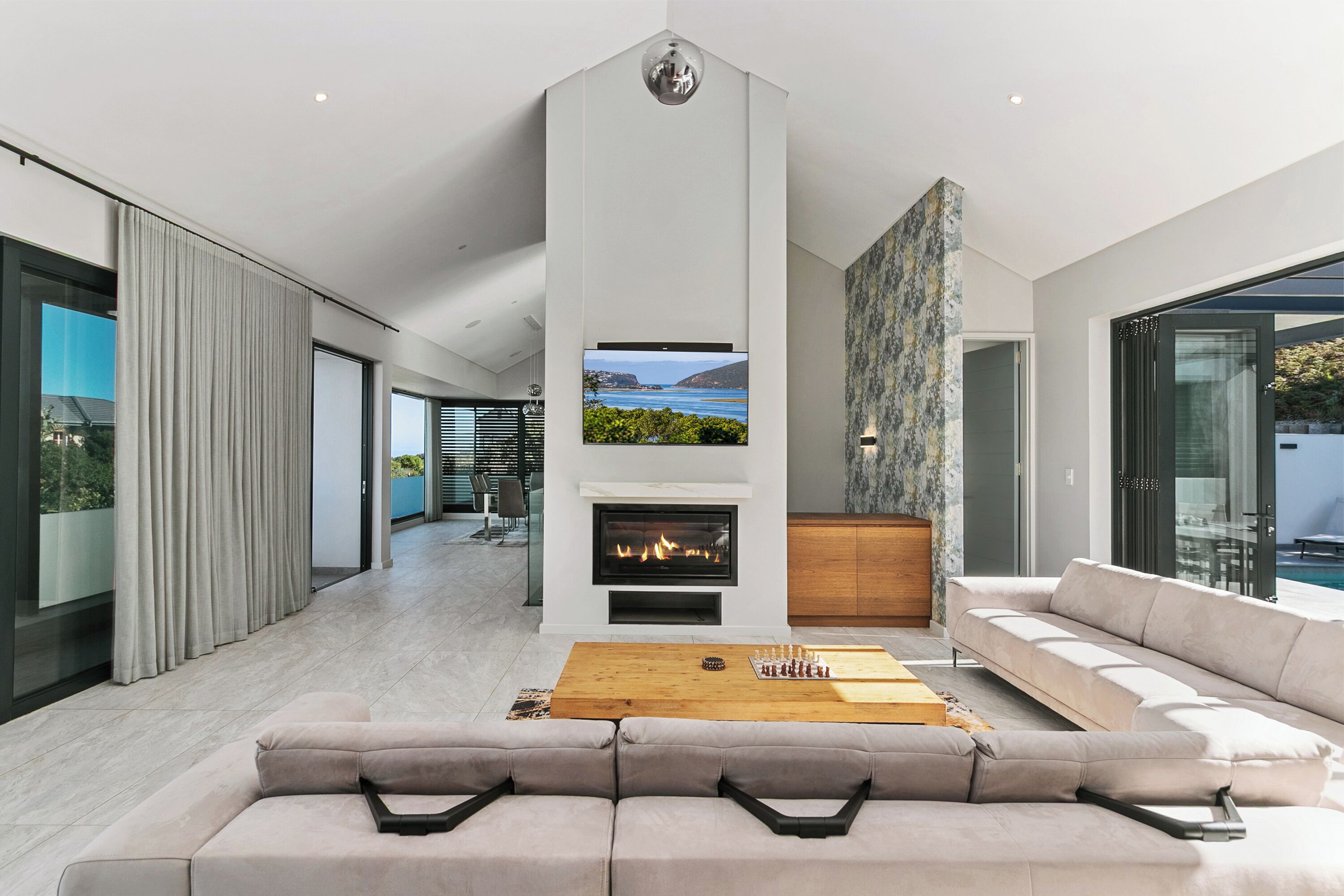 A modern living room with a fireplace, a large window with a view, and a sofa.
