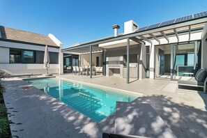 A modern outdoor pool area with a covered patio, seating, and a clear sky. - Miles End @ Pezula (Knysna)