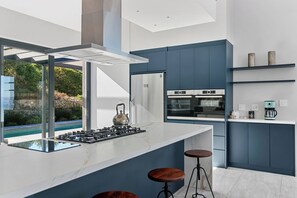 A modern kitchen with a gas stove, stainless steel appliances, and a view of a pool. - Miles End @ Pezula (Knysna)