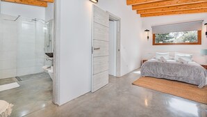 A modern bedroom with a large bed, a walk-in closet, and a bathroom with a glass shower enclosure. - Cosy 2-bed Villa With Pool, Pollenca (Pollença)