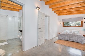 Ein modernes Schlafzimmer mit einem großen Bett, einem begehbaren Kleiderschrank und einem Badezimmer mit einer Duschkabine aus Glas.