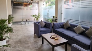 Un espace de vie moderne comprenant un canapé, des fauteuils et une table basse. On y trouve également des plantes en pot et une vue sur l’extérieur.