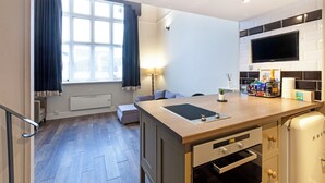 A modern kitchen with a built-in stove, a flat-screen TV, and a window with curtains. - One Bedroom Duplex in Paddington (London)