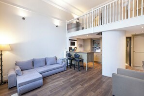 A modern living room with a grey sectional sofa, a dining area with bar stools, and a kitchen with a central island. - One Bedroom Duplex in Paddington (London)