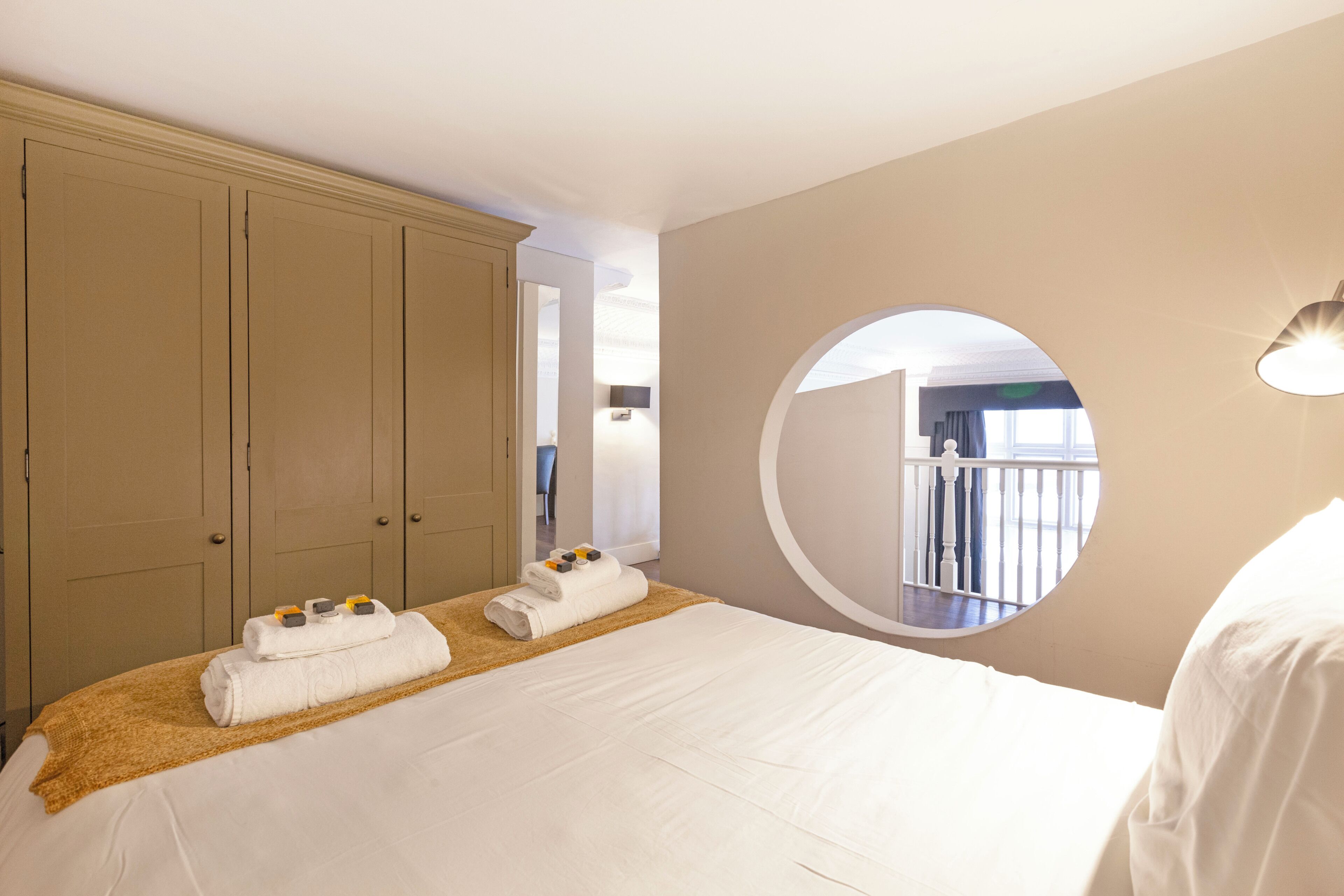 Ein Hotelzimmer mit einem großen Bett, einem Kleiderschrank, einem runden Spiegel und Blick auf den Balkon.