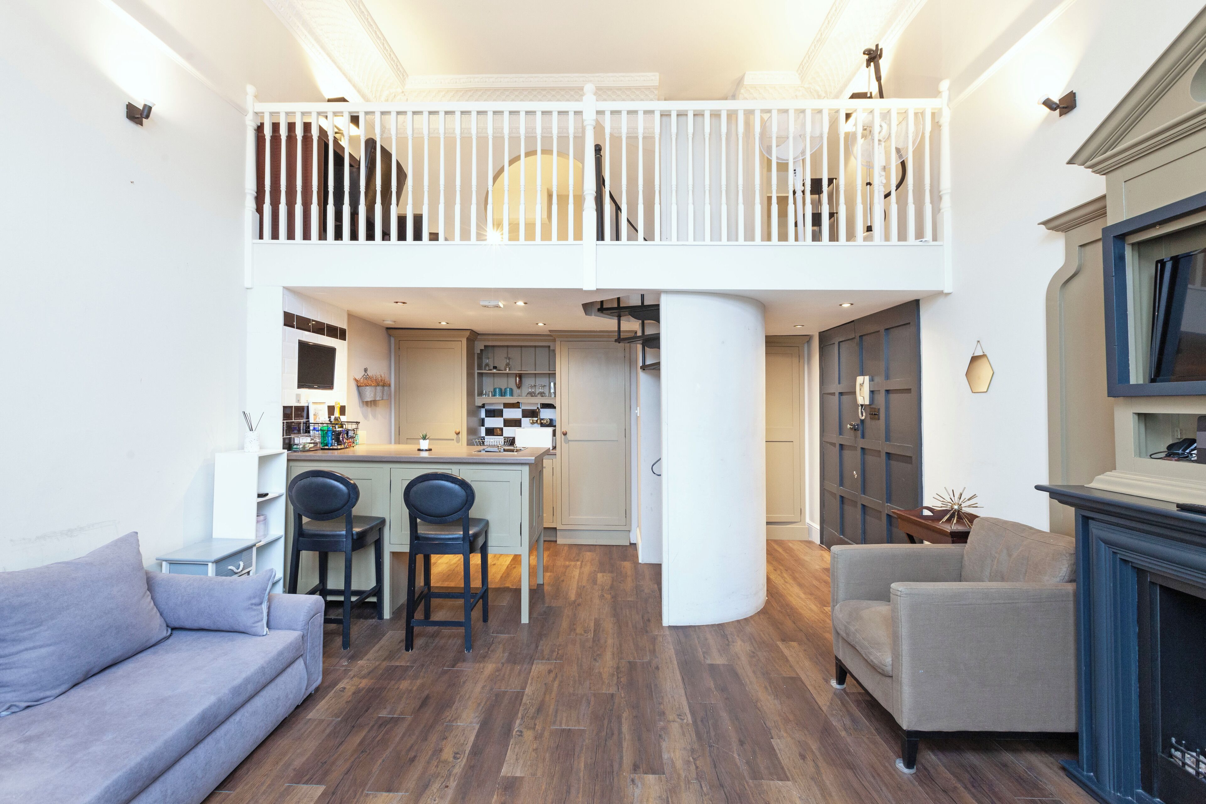 A spacious living area with a high ceiling, a dining area with two chairs, a sofa, and a fireplace.
