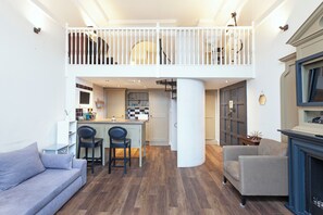 A spacious living area with a high ceiling, a dining area with two chairs, a sofa, and a fireplace. - One Bedroom Duplex in Paddington (London)