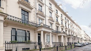 A row of white buildings with black railings and columns, parked cars, and a clear sky. - One Bedroom Duplex in Paddington (London)
