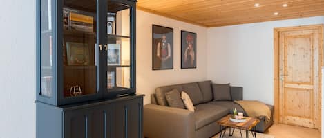 A living room with a dark wooden cabinet, a grey sofa, and two framed pictures on the wall.