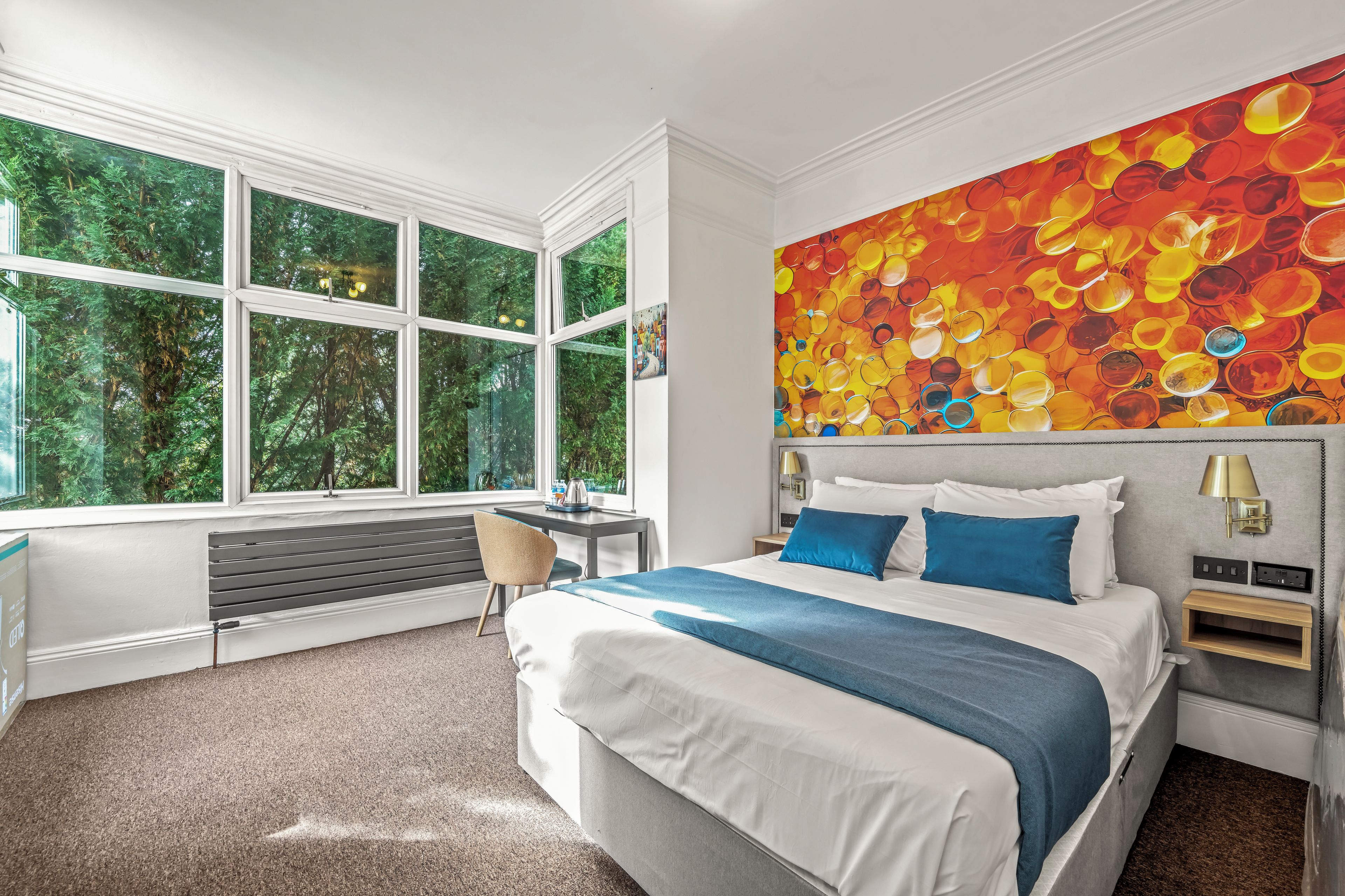 Une chambre d’hôtel moderne, dotée d’un grand lit, d’un bureau et offrant une vue sur la verdure grâce à de grandes fenêtres.