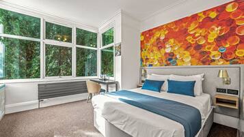 Una habitación de hotel moderna con una cama grande, un escritorio y vistas a zonas verdes a través de amplias ventanas.