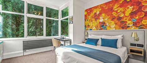 Una habitación de hotel moderna con una cama grande, un escritorio y vistas a zonas verdes a través de amplias ventanas.