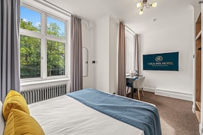 A hotel room with a bed, a desk, and a view of trees through the window. - Seka Inn Hotel (Crowthorne)